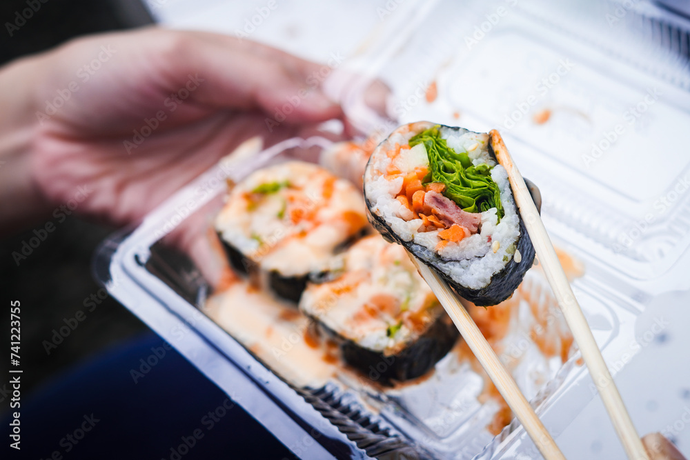 Indonesian street food sushi, illustration of hand holding sushi with chopsticks Indonesian street food sushi, illustration of hand holding sushi with chopsticks