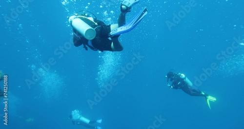 A group of divers diving towards a sunken ship in the Philippine Sea. Divers descend together around a guide rope. Divers descend into a cloud of bubbles. Summer vacation shot