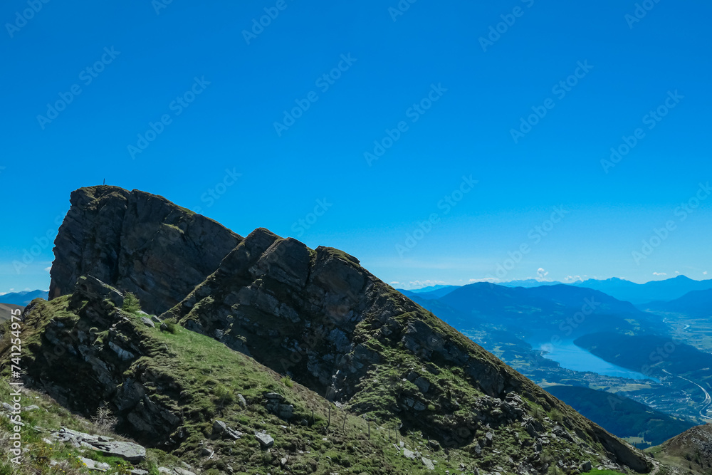 Obraz premium Idyllic hiking trail on alpine meadow with scenic view of lake Millstatt seen from mountain peak Boese Nase in Ankogel Group, Carinthia, Austria. Remote landscape in majestic Austrian Alps in summer