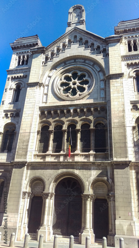 Neo-Gothic building with arched windows and a flag on a sunny day.