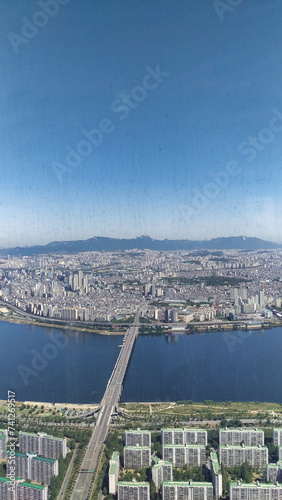 A panoramic aerial view of a city with a river and a long bridge crossing it.