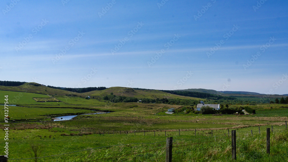 Expansive rural landscape with a winding stream, green fields, and a blue sky, evoking a sense of tranquility.