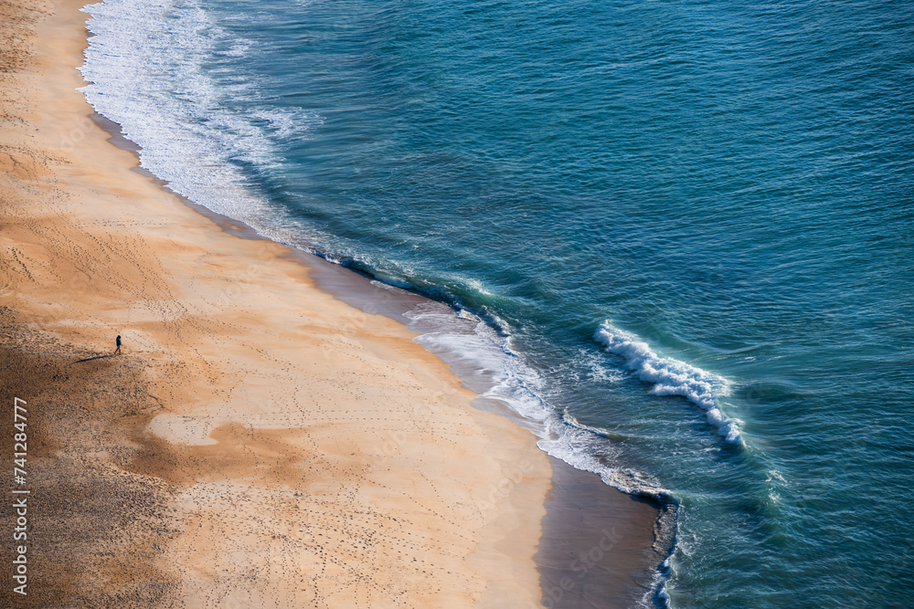 Man walking on the beach at sunset. Atlantic ocean coast in Nazare, Portugal.