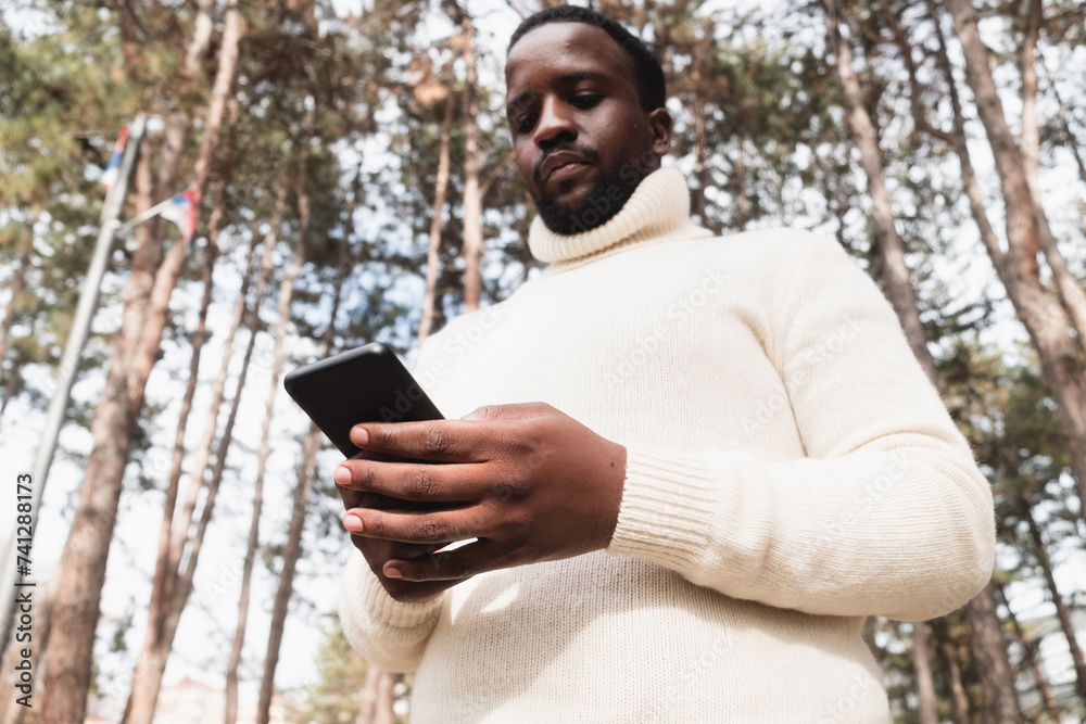 Fototapeta premium Young black man yuppie hipster in a park using a mobile phone