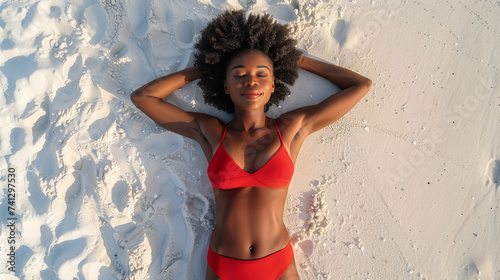 Top down view of a black African American beautiful young woman sunbathing in swimwear on a white sand beach on sunny summer day