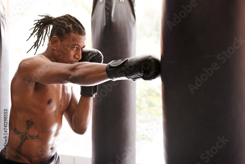 Muscle, punching bag and black man in gym for exercise, boxing challenge or competition training. Power, fitness and serious champion boxer at workout with confidence, fight and energy in sports club