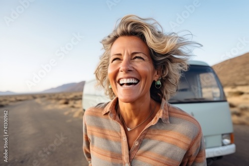 Mature woman laughing in front of camper van in the desert