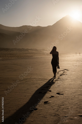 Chica con un vestido caminando por la playa de Cofete en Fuerteventura con los zapatos en la mano photo