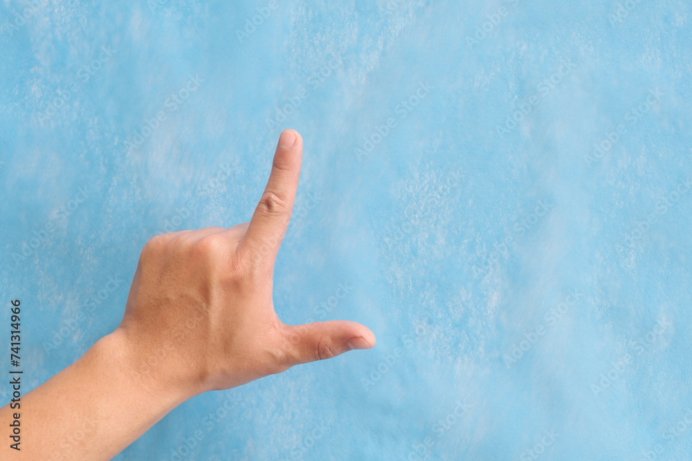 Young male Asian hand making loser sign or letter L isolated on blue background.