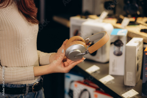 Photos girl standing in front of the stand in the electronics store chooses headphones