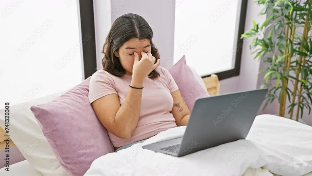 Hispanic woman feeling stressed while using laptop in her bedroom at home.