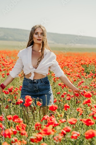 Happy woman in a poppy field in a white shirt and denim skirt with a wreath of poppies on her head posing and enjoying the poppy field.