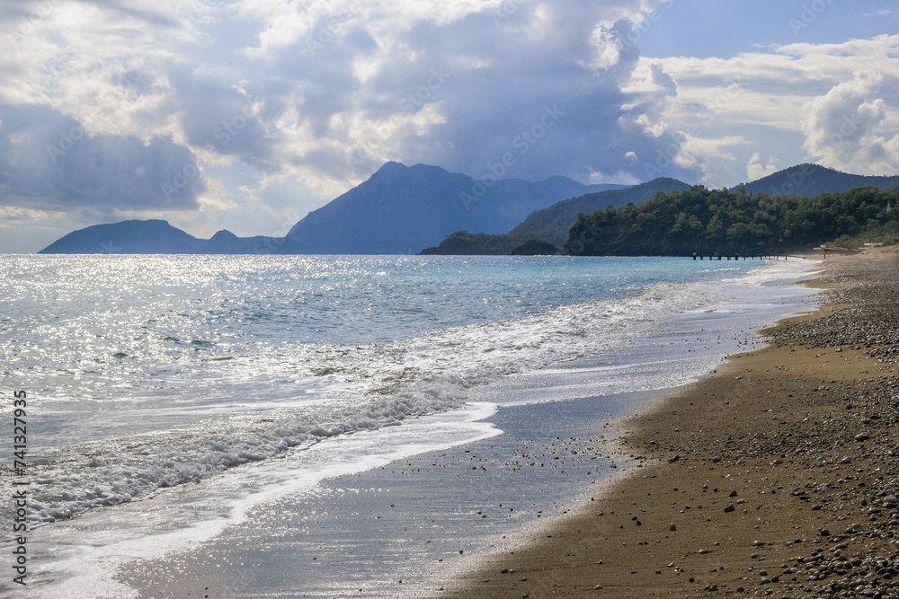 Beautiful Beach Scene with Mountain, Soft Sand, Waves, and Cloudy Sky Set Against Bright Sunlight