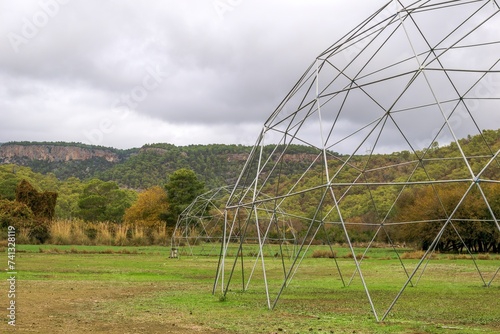 Fotografie Large metal geodesic dome greenhouse structure in a rural setting with hills in
