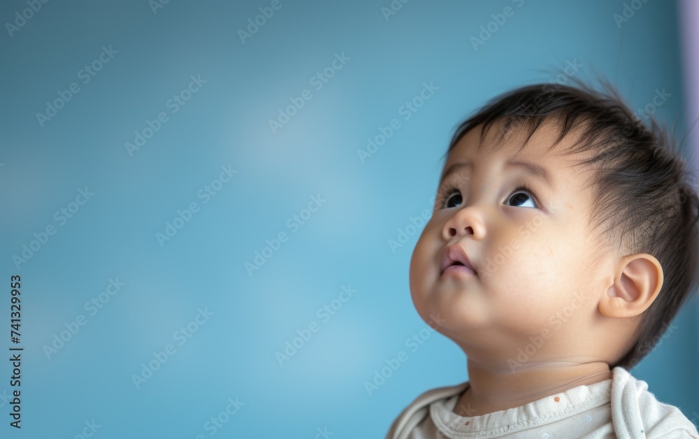A multiracial baby with wide eyes looks up against a blue background, showing curiosity and wonder A multiracial baby with wide eyes looks up against a blue background, showing curiosity and wonder