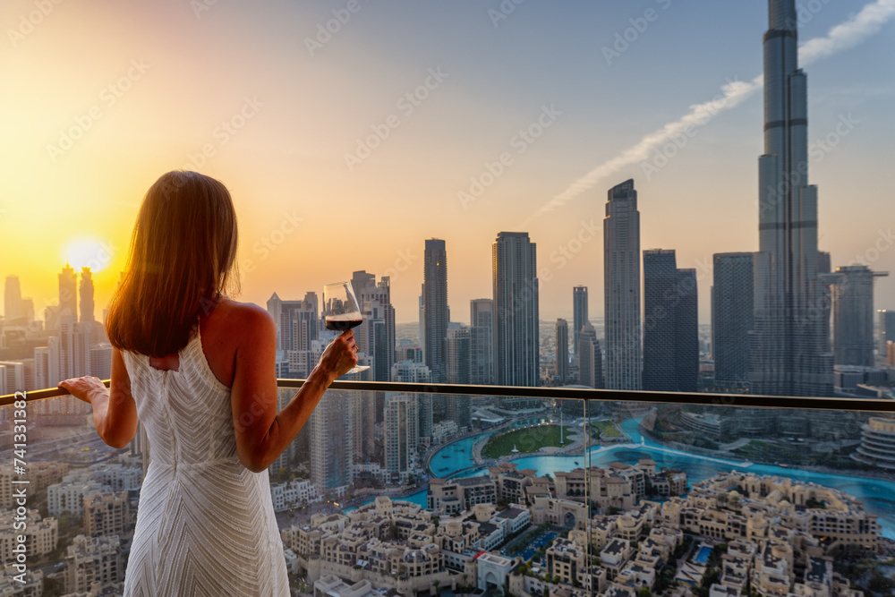 A beautiful woman enjoys the panoramic sunset view over the skyline of Downtown Dubai, UAE, with a drink in her hand A beautiful woman enjoys the panoramic sunset view over the skyline of Downtown Dubai, UAE, with a drink in her hand