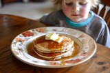child with a plate of pancakes topped with syrup and butter