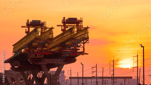 Silhouette metal launching gantry structure for installing concrete typical segment joint on foundation of elevated expressway on highway in under construction against sunset sky background  photo