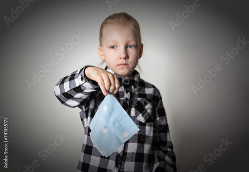 a sad girl aged seven years old holds a handkerchief in her hand against the background of a plaid shirt. Concept of runny nose and nasal congestion in children. Chronic rhinitis and sinusitis. \