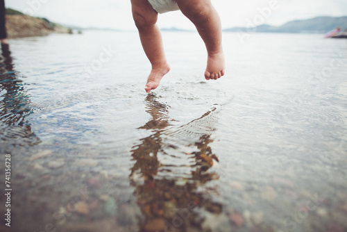 A baby is playfully jumping into the liquid with a diaper on at the beach photo