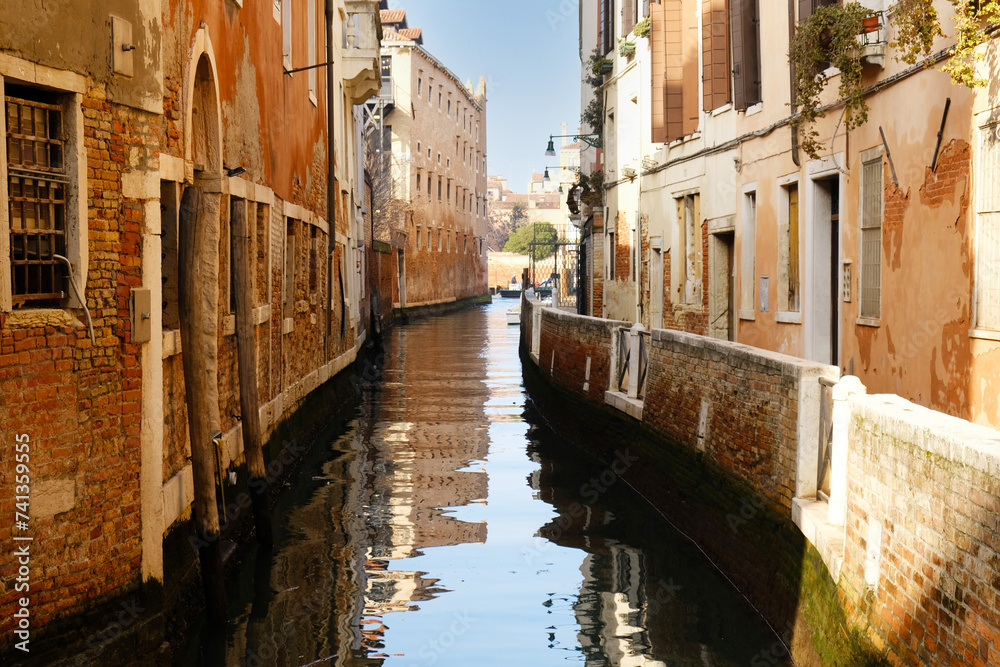 Typical narrow streets and canals between сolorful and shabby houses in Venice, Italy. Historical architecture in Venice, parked boats on the canals.