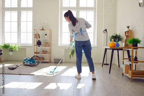 Obraz na plátne Smiling young woman housewife mopping the floor in the living room at home with detergent