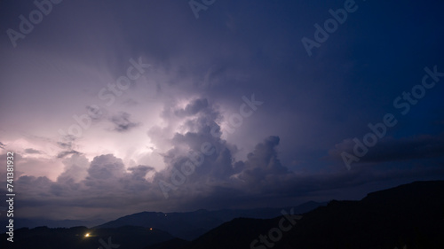 Evening thunderstorm with lightning in the mountains. Dramatic clouds during a thunderstorm pierce the light of lightning in a mountainous area. © Niko_Dali