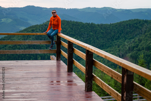 a young girl sits on a wooden handrail. photo