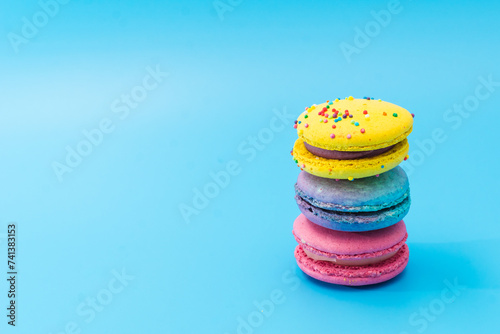 Brightly colored stacked macarons on blue background. Tasty colorful macaroon assorted. French pastry made from egg whites. Culinary, cooking concept.