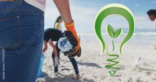 Image of go green light bulb logo over diverse group picking up rubbish from beach