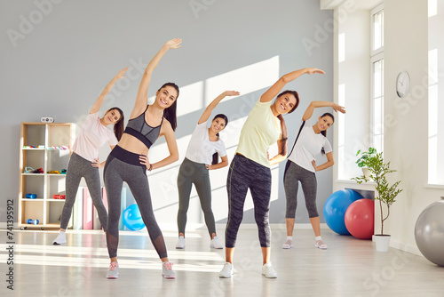 Group of happy smiling young beautiful women doing stretching exercises at a fitness workout at a modern gym. Sport, working out, wellness, healthy lifestyle concept