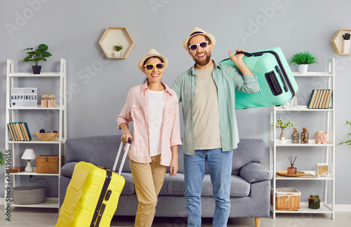 Happy cheerful smiling loving married couple with packed up suitcases ready for summer holiday standing together in living room at home. Traveling, vacation concept  © Studio Romantic