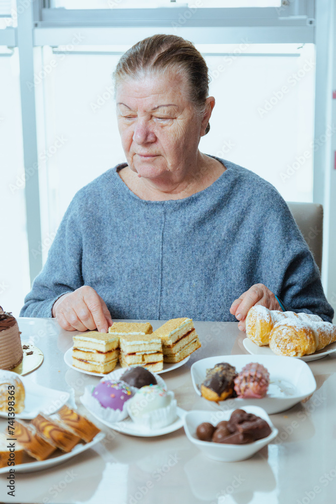 Aged woman pensioner eating chocolate donut and sweet food, unhealthy eating for retired people. Happy grandmother eating food with sugar while her grandchildren out. Aged woman pensioner eating chocolate donut and sweet food, unhealthy eating for retired people. Happy grandmother eating food with sugar while her grandchildren out.