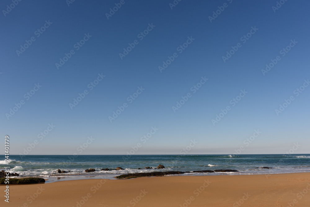 Línea del horizonte separando el cielo azul y el mar, con una débil bruma., Vista desde una playa con arena mojada. 