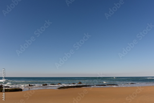 L  nea del horizonte separando el cielo azul y el mar  con una d  bil bruma.  Vista desde una playa con arena mojada. 