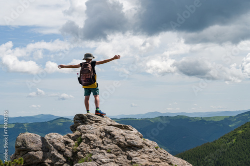 A schoolboy boy stands on a stone with his arm outstretched against the background of the Ukrainian Carpathians.