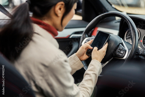 Selective focus on japanese woman's hands typing message in her car.