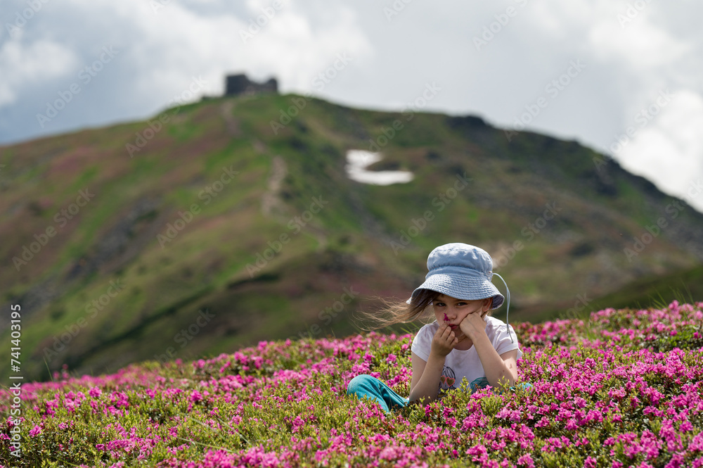 A little girl is sitting on a lawn full of rhododendrons.