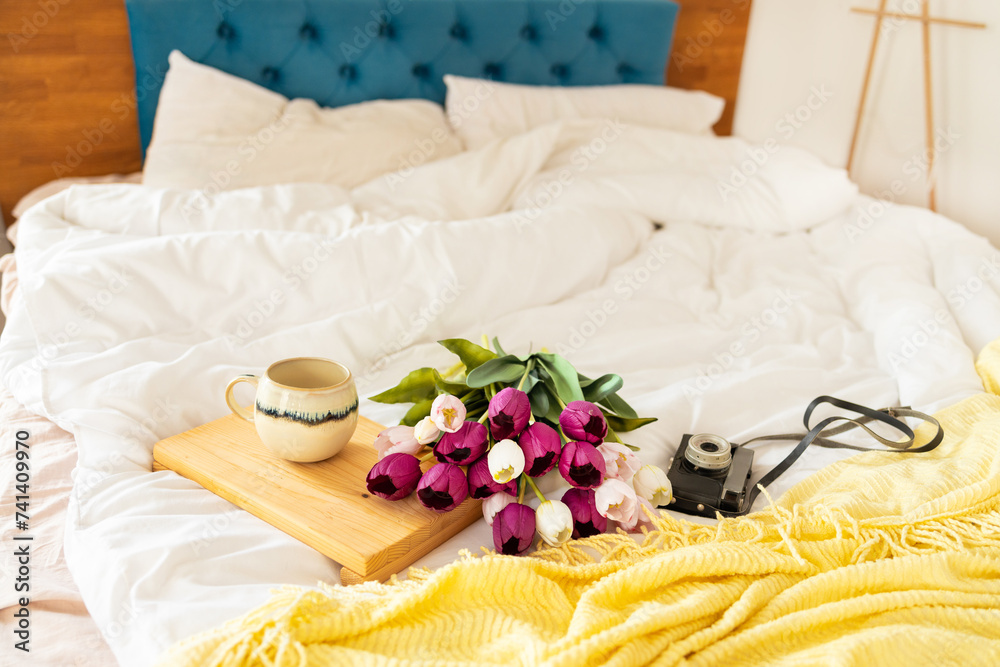 Coffee cup and bouquet of tulips on the bed