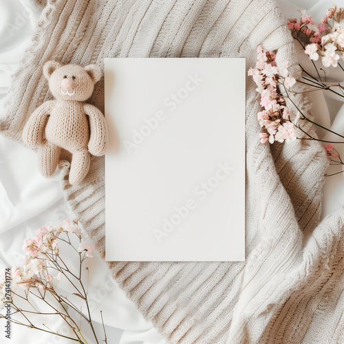 Top view of teddy bear beside blank paper with pink blossoms, ideal for invitations.