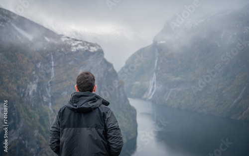 Traveler with his back turned, enjoying a mountain landscape in the Norwegian fjords of Geiranger, Norway.	