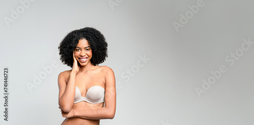 African-American woman laughs, stands in a strapless top, her arms crossed in a relaxed manner, against a neutral backdrop, encapsulating the spirit of carefree elegance and infectious cheerfulness