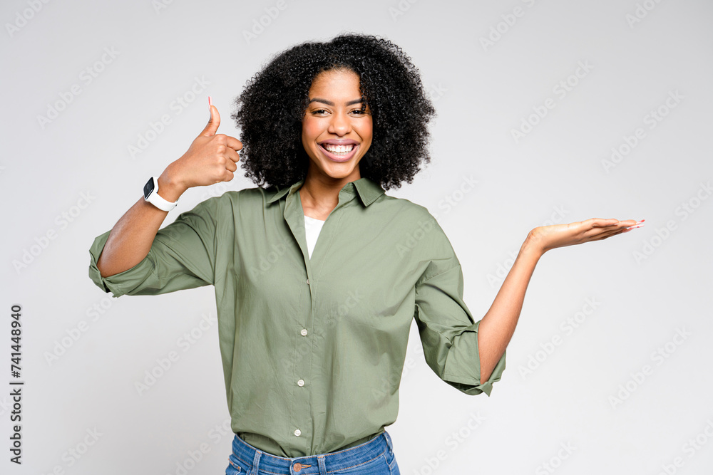 An exuberant African-American woman with curly hair smiles widely, giving a thumbs-up with her right hand while her left hand is open as if presenting, recommending or approving something