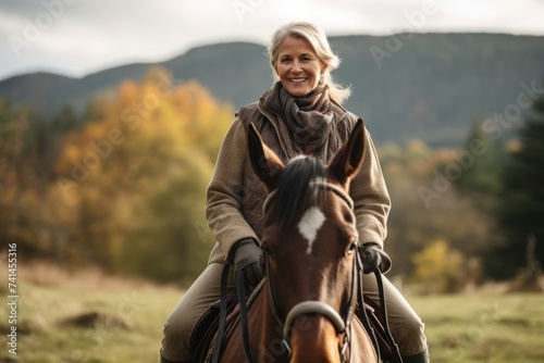 Senior woman riding a horse in the autumn forest. Outdoor portrait.
