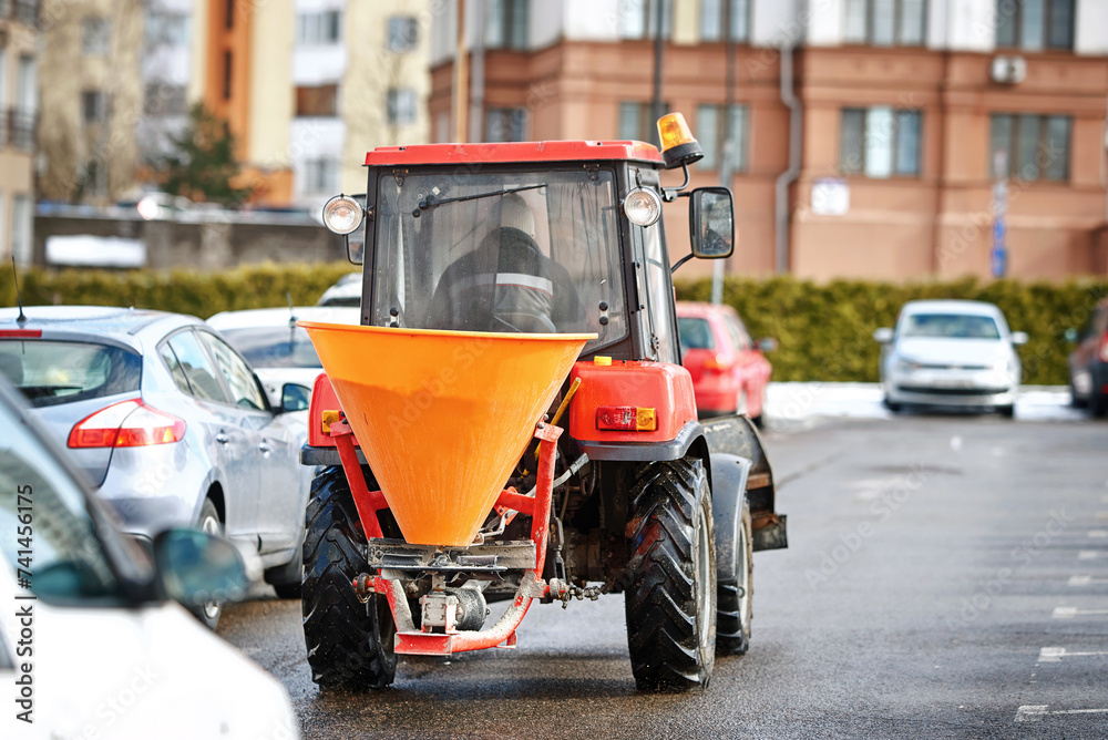Tractor with salt spreader driving on city road, snow management. Tractor with salt and sand