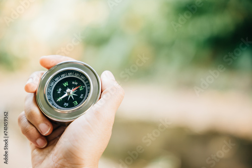 In the forest a hiker uses a compass to conquer confusion and find direction. The compass in the traveler hand represents topography and discovery amidst nature beauty.