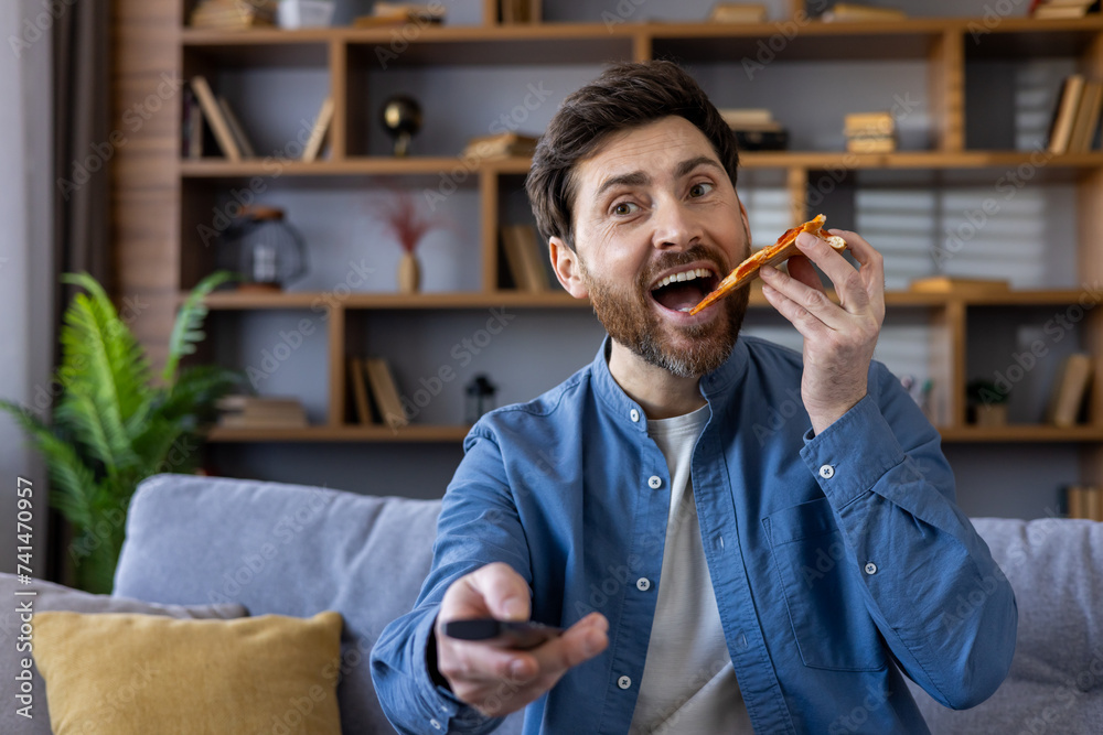 © Liubomir - Casual bearded man eating pizza and watching tv, enjoying a relaxed evening at home alone © Liubomir - Casual bearded man eating pizza and watching tv, enjoying a relaxed evening at home alone