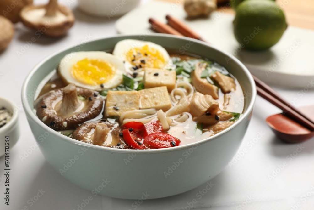 Noodle soup. Bowl of delicious ramen, ingredients and chopsticks on white tiled table, closeup