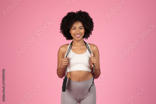 Fototapeta Naklejka Na Ścianę i Meble -  Happy black fitness woman with jump rope on pink backdrop
