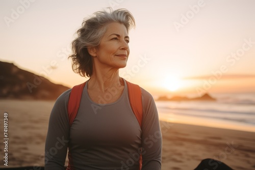 Portrait of active senior woman looking away while standing on beach at sunrise